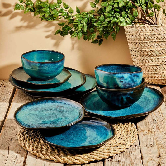 Set of blue ceramic bowls and plates on a wooden surface with a plant in the background.