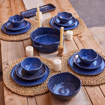 Set of blue stardust ceramic dinnerware dishes on a wooden table with candles and placemats.