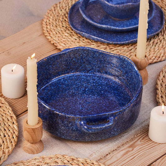 Blue Stardust ceramic tajin with wooden handles on a table with candles and placemats.