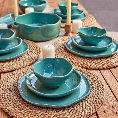Handmade jade dinnerware set, featuring wavy-edged bowls and plates on woven placemats with candles.
