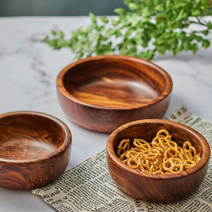 Three wooden bowls on a textured surface with a plant in the background