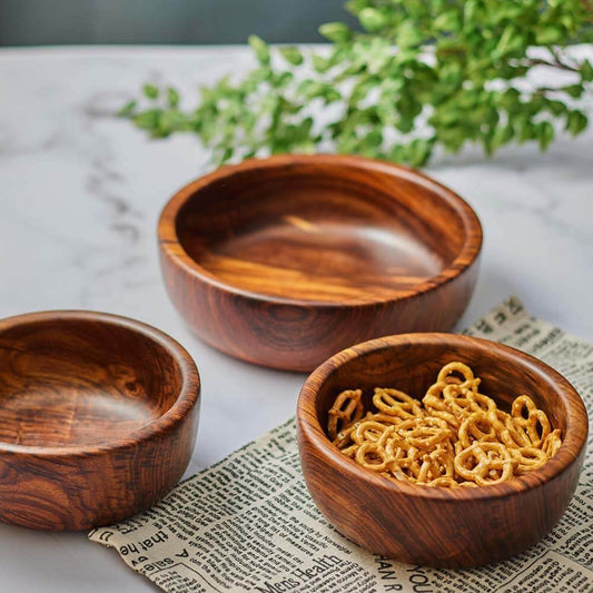 Three wooden bowls on a textured surface with a plant in the background