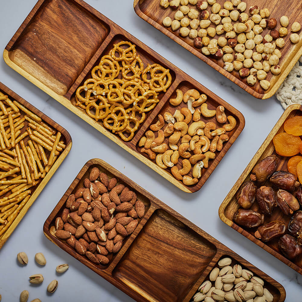 Wooden serving tray filled with nuts, pretzels, dried fruits, and snacks arranged neatly in divided sections.