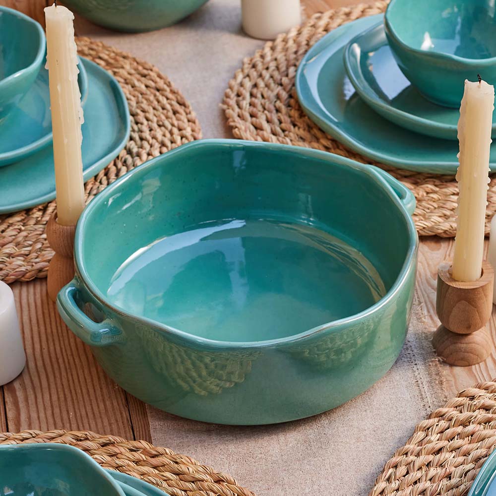 A Jade Tajin on a wooden table with a woven placemat and white candles in the background.