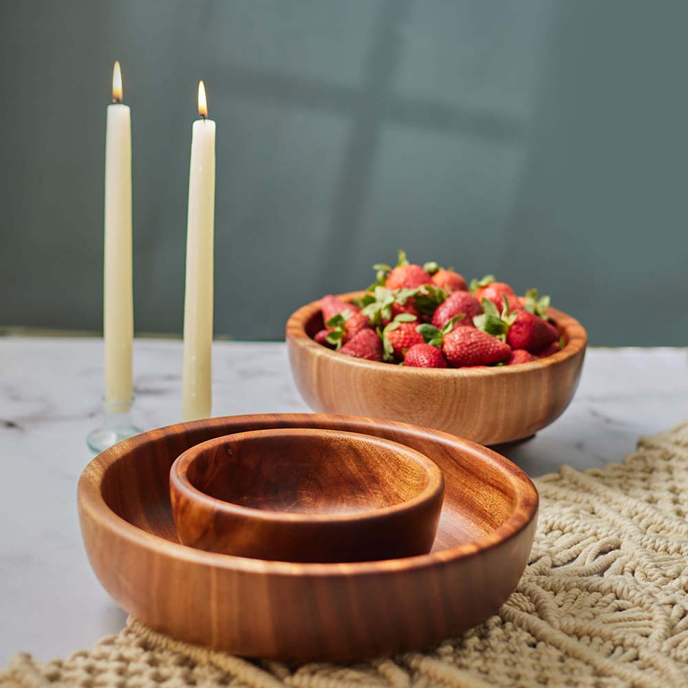 Wooden bowls with strawberries and candles on a marble countertop.