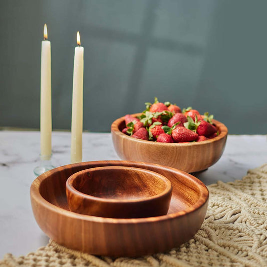 Wooden bowls with strawberries and candles on a marble countertop.