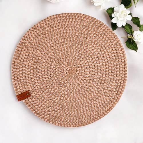 Round woven mat with a brown leather tag on a white surface with flowers.