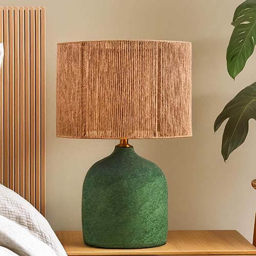 Handmade Boho-style Verra lamp with a textured green ceramic base and woven brown shade on a wooden nightstand.