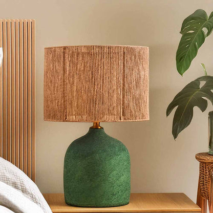 Handmade Boho-style Verra lamp with a textured green ceramic base and woven brown shade on a wooden nightstand.